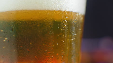 Macro-shot-of-a-drop-running-over-a-glass-of-beer.-Sweat-on-a-cold-glass-of-beer.-A-dripping-drop-on-a-glass-filled-with-beer.